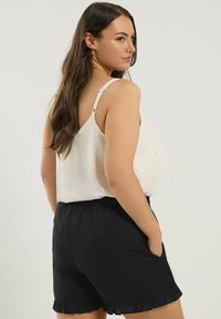 Satin cami-topp i krämfärg med justerbara axelband, i kombination med svarta shorts med volangkant och elastisk midja.