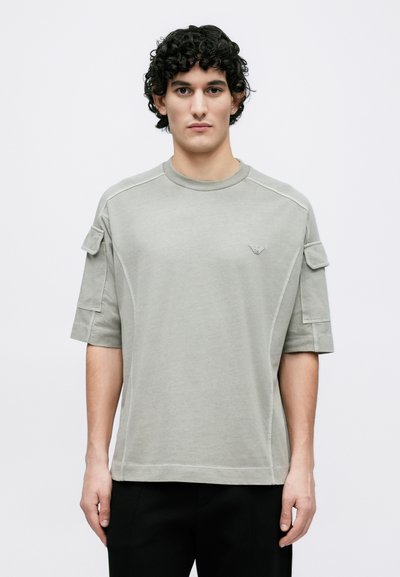 Ανοιχτό γκρι κοντομάνικο μπλουζάκι από μαλακό βαμβάκι, με τσέπες στους ώμους και διακριτικό λογότυπο στο αριστερό στήθος.