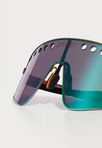 Ochelari de soare multicolori cu un design mare al vizorului, prezentând o lentilă cu gradient și un cadru metalic. Orificiile de-a lungul marginii superioare adaugă detalii.