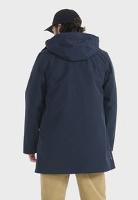 Parka impermeabile blu con cappuccio, progettata con una texture liscia e maniche lunghe, che si estende sotto la vita, con una branding discreta.