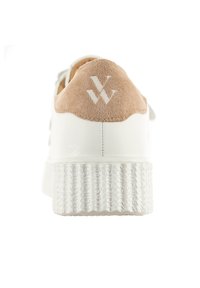 Baskets blanches avec un talon en suede beige, semelle en caoutchouc texturée et un logo en relief à l'arrière. Cuir lisse et matériaux doux utilisés.