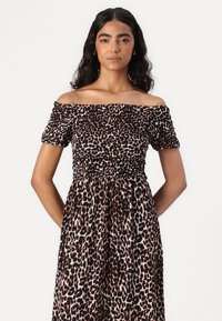 Off-shoulder klänning med leopardmönster som har en figurnära överdel med rynkad detalj, korta ärmar och en flödande långkjol som når anklarna.