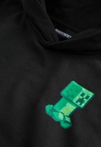 Sudadera con capucha negra que presenta un personaje Creeper pixelado en verde de Minecraft en la parte frontal. Tela suave, corte relajado, sin herrajes visibles.