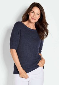 Marineblauer Strickpullover mit weitem Ausschnitt und kurzen Ärmeln. Der Stoff hat eine strukturierte Optik. Kombiniert mit weißen Hosen.