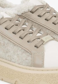 Beżowe sneakersy z futrzanym tekstylnym fragmentem, skórzanymi akcentami i teksturowaną gumową podeszwą. Cechy to sznurówki i małe logo.