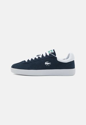 Navy skinnesneakers med hvit gummisåle, hvite snøringer og grønn/hvit logodetalj. Glatt tekstur og klassisk lavprofil design.