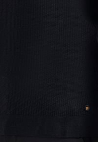 Zwarte gebreide trui met een geweven patroon, geribde zoom en een klein merkaccent aan de onderkant.