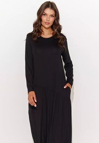Czarna sukienka z długim rękawem i okrągłym dekoltem, wykonana z miękkiego materiału. Posiada zwiewny fason z delikatnymi zakładkami i bocznymi kieszeniami.