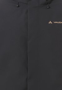 Schwarze Oberbekleidung mit einer glatten, matten Textur und kontrastierendem Logo. Verfügt über eine verstellbare Kapuze und einen Frontreißverschluss. Sauberes, minimalistisches Design.