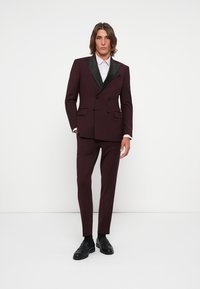 Burgundy two-piece suit with black satin lapel, double-breasted jacket, tailored fit, slim trousers, and black shoes. Smooth fabric texture.