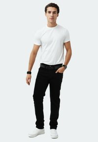 Weißes Kurzarm-T-Shirt, schwarze Slim-Fit-Jeans, schwarzer Gürtel und weiße Sneaker. Legere Kleidung mit einer figurbetonten Passform.