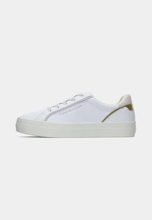 White canvas sneaker with white rubber sole, round toe, lace-up design, featuring a gold accent at the heel and brand logo embossed on the side.