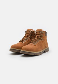 Botas de ante marrón con un cuello acolchado, cordones texturizados, ojales de metal y una suela de goma resistente con surcos profundos para el agarre.