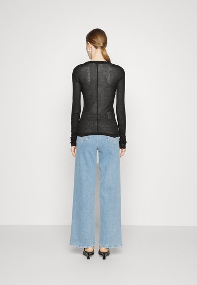 Black long-sleeve top with a fitted design and textured fabric, paired with light blue wide-leg jeans and black heels.