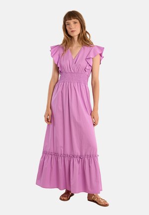 Donna che indossa un abito lungo lavanda senza maniche con spalle e vita arricciate, abbinato a sandali piatti marroni.