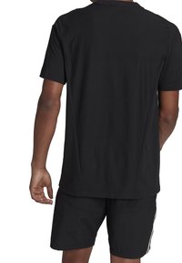 Man som bär en enkel svart t-shirt med kort ärm och svarta shorts med vita ränder, visad bakifrån mot en vit bakgrund.