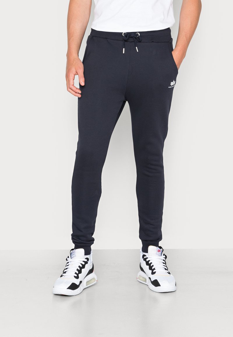 Marineblå joggers med en slank pasform, snor i taljen, forlommer og en hvid logo-detail på det øverste venstre ben. Materialet er blødt og strækbart.