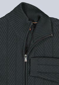 Dunkelgrauer Strickpullover mit einem gerippten Schalkragen, Zickzackmuster, sichtbarem silbernen Reißverschluss und umgeschlagenen Ärmeln auf einem hellen Hintergrund.