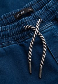 Blå jogging-shorts lavet af denim med elastisk taljebånd og en sort-hvid flettet snor med mærkede ender.