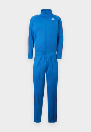 Μπλε φόρμα με φερμουάρ σε όλο το μήκος, με λευκό λογότυπο στο στήθος και ριγέ λευκό-μπλε σχέδιο που κυλάει κατά μήκος των μανικιών και των ποδιών του παντελονιού.