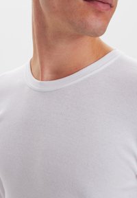 White, ribbed crew neck t-shirt with short sleeves, made from a smooth, stretchable fabric. Close-up of collar and upper chest area.