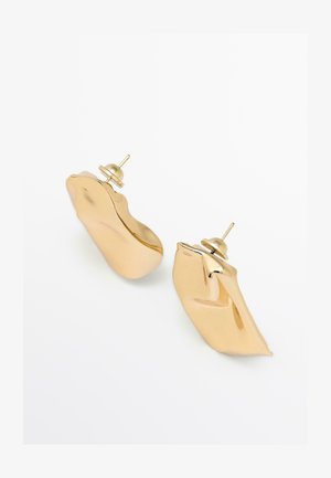 Náušnice z kovu ve zlaté barvě s vlnitým, abstraktním designem. Bezpečné zapínání s malým kolíčkem. Hladký, reflexní povrch.