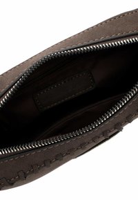 Ruda zomšos pagaminta kišenė su užtrauktuku, pasižyminti kontrastinga siuvimo linija ir lygiu vidiniu pamušalu. Minimalistinis dizainas be papildomų detalių.