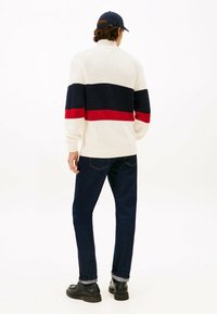 Sweter dzianinowy w kolorze kremowym z poziomymi paskami w granatowym i czerwonym kolorze, z wysokim kołnierzem i ściągaczami na rękawach. Połączony z ciemnymi dżinsami i czarnymi butami.