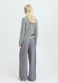 Grauer Strickpullover mit geripptem Saum, kombiniert mit grauen, weit geschnittenen Hosen in feinem Muster, die einen lockeren Sitz und eine weiche Textur bieten.