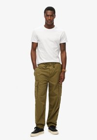 Olijfgroene cargobroek met meerdere zakken, elastische boorden en een trekkoord in de taille, gecombineerd met een eenvoudig wit T-shirt en zwarte sneakers.