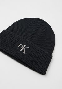 Μαύρο πλεκτό σκουφάκι με ραχιαία υφή, διαθέτει διπλωμένο γείσο και ραμμένο λογότυπο 'cK' σε ασημί χρώμα μπροστά.