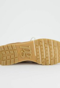 Sneaker marron clair avec une semelle en caoutchouc texturée, présentant un motif de rainures et de points pour une meilleure adhérence. Lacets blancs et détail du logo visibles.