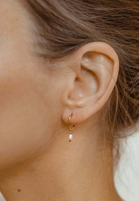 Orecchino a cerchio dorato con una piccola goccia di perla, design delicato, superficie liscia e finitura lucida, indossato su un orecchio.