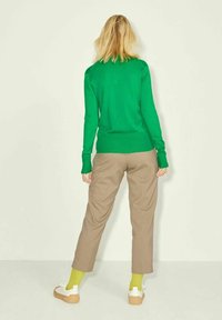 Grön stickad tröja, beiga byxor och vita sneakers med bruna sulor. Outfiten har en avslappnad passform och långa ärmar med ribbade manschetter.