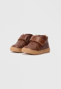 Sapatos de couro castanho com uma tira de velcro, bico arredondado e sola de borracha. Forro em fleece no tornozelo para conforto. Design casual.