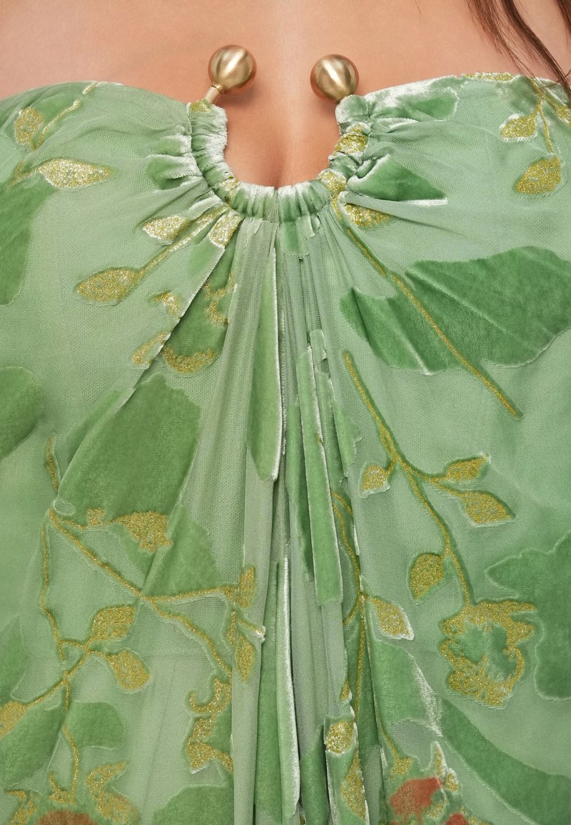 Green velvet dress with gold floral patterns, featuring a gathered neckline held by two large gold bead clasps.