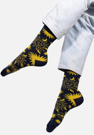 Granatowe skarpetki z żółtymi wzorami słońca i gwiazd, wykonane z miękkiego materiału z dopasowanym krojem, podkreślające unikalne motywy związane z niebem.