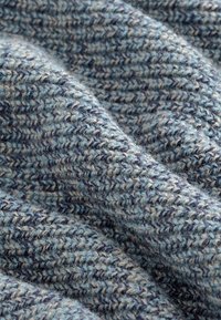 Primo piano di un tessuto testurizzato con un motivo a maglia blu e grigio, che mostra filato morbido e leggermente peloso e pieghe delicate.