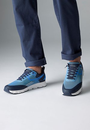 Des chaussures de sport bleues avec un mélange de textures lisses et en maille, dotées d'une semelle rembourrée, d'accents bleu foncé contrastants et de détails gris.