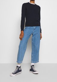 Marinblå tröja med spetskrage, ljusblå vida jeans och marinblå höga sneakers. Materialet verkar mjukt med en slät yta.