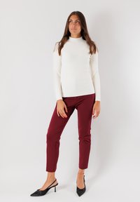 Maglione bianco a collo alto con coste abbinato a pantaloni aderenti bordeaux e décolleté nere a punta. L'insieme presenta linee pulite e una silhouette elegante.