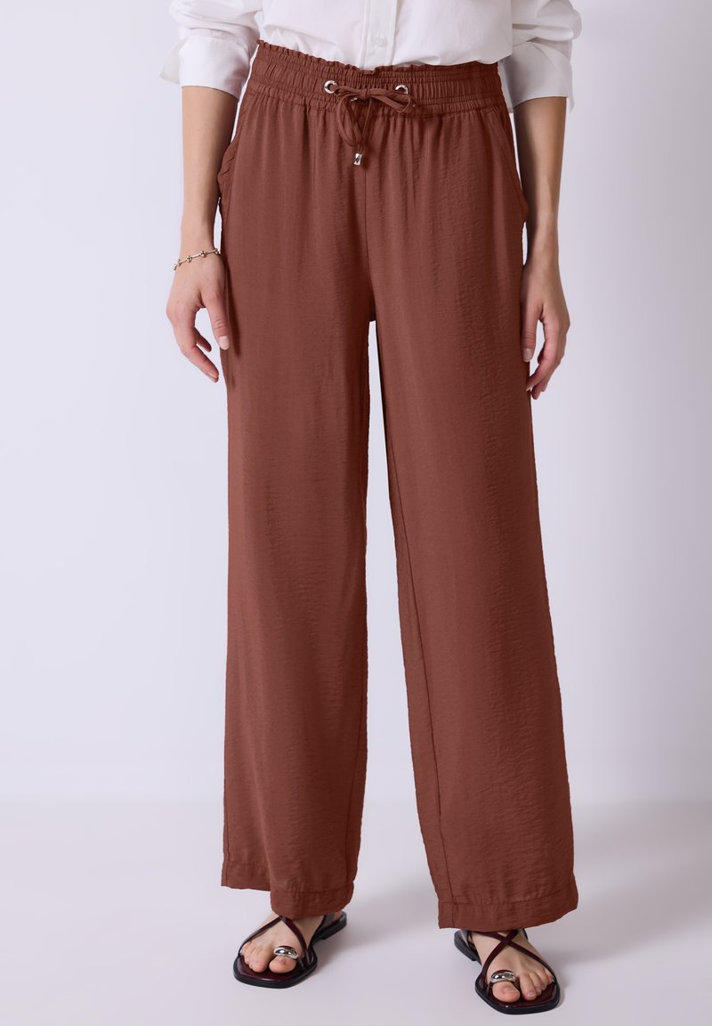 Bruine wijde broek met een elastische tailleband en trekkoord. Gestructureerde stof, zijzakken, gecombineerd met zwarte sandalen.
