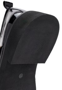 Chaussure en cuir verni noir avec une semelle en caoutchouc noir texturée, présentant des rainures horizontales et un petit talon. Design à bout arrondi.