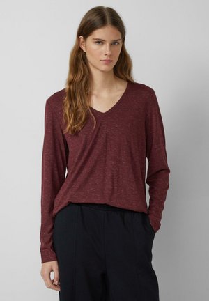 Bordeaux lange mouwen t-shirt met een v-hals, met een relaxte pasvorm en subtiele gemêleerde textuur. Gecombineerd met donkere broek.