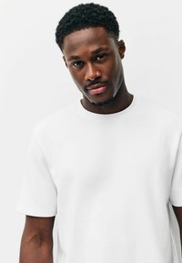 Fehér pamut póló kerek nyakkivágással és rövid ujjakkal, laza szabással és sima textúrával. Egyszerű és letisztult dizájn.