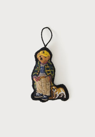 Porte-clés brodé d'un ours portant une casquette jaune, une veste, un pantalon cargo et des baskets, debout avec un petit chien en laisse.
