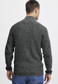 Suéter de punto texturizado en blanco y negro con cuello alto, mangas largas y cintura ajustada, visto desde la parte posterior.