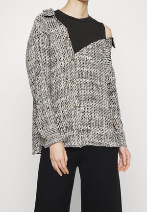 Person wearing an off-shoulder black sleeveless top under a gray and black tweed buttoned jacket paired with black pants.