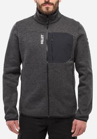 Veste en polaire grise avec un col haut, une fermeture éclair à l'avant et une poche poitrine noire. Présente un tissu texturé et un passepoil contrastant.