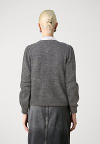 Grijze gebreide trui met opgeblazen mouwen, geribbelde zoom en detail aan de achterkant van de hals, gecombineerd met een donkere denim rok. Gladde textuur.